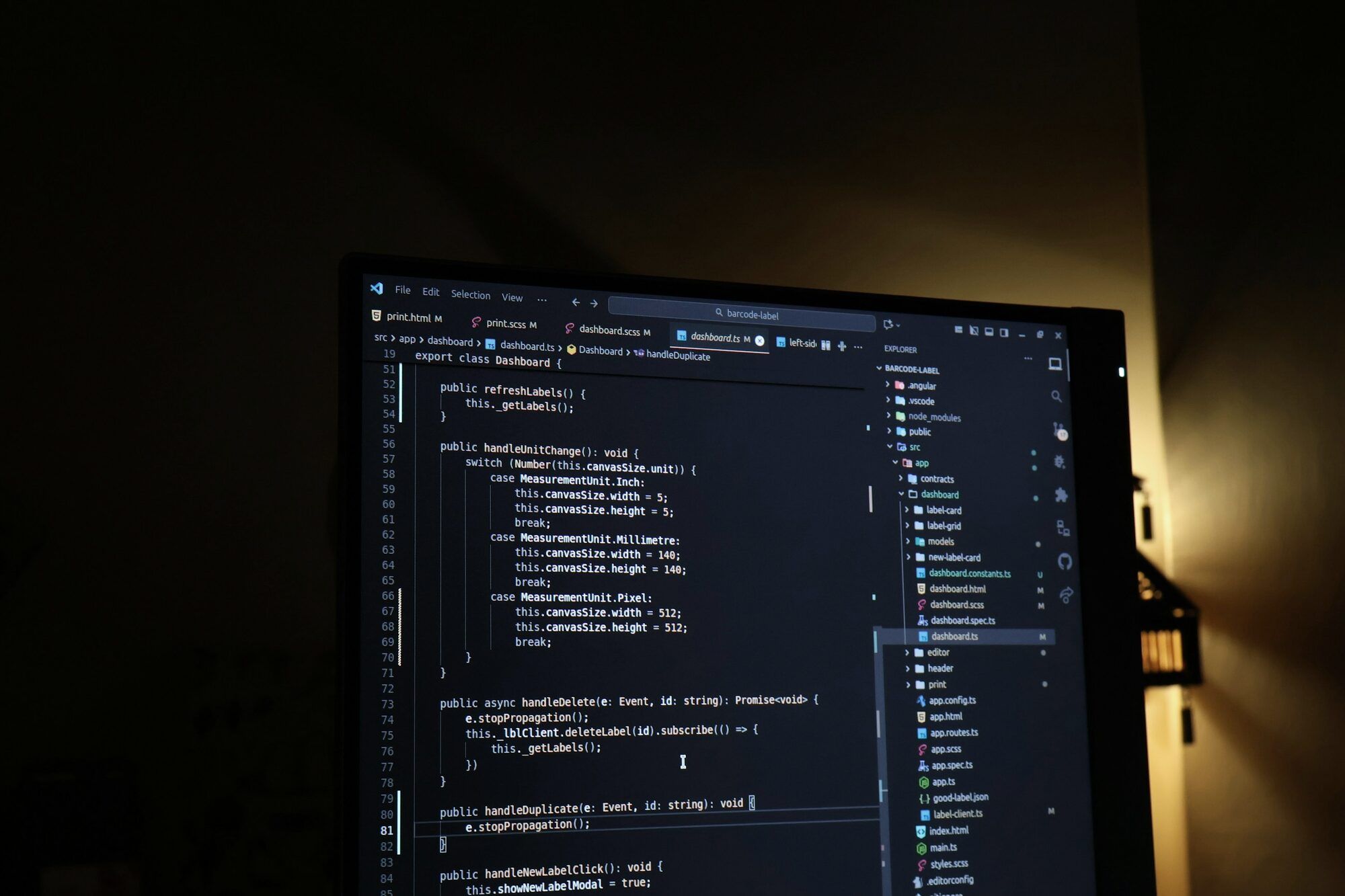 Monitor con código abierto en un editor, en una sala a oscuras con una luz cálida al fondo