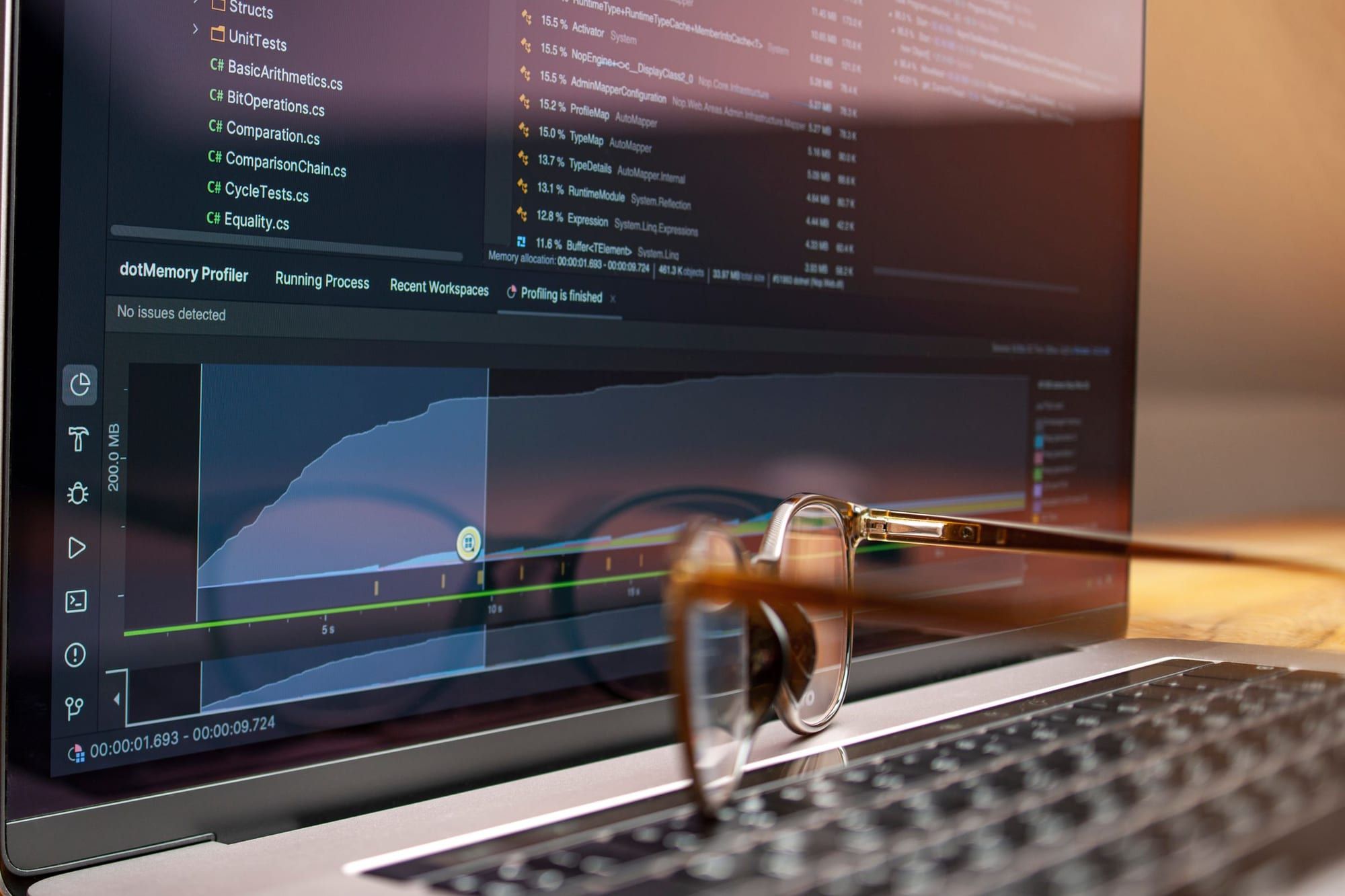 Portátil con un perfilador de memoria y una gráfica de consumo en pantalla, con unas gafas apoyadas en el teclado