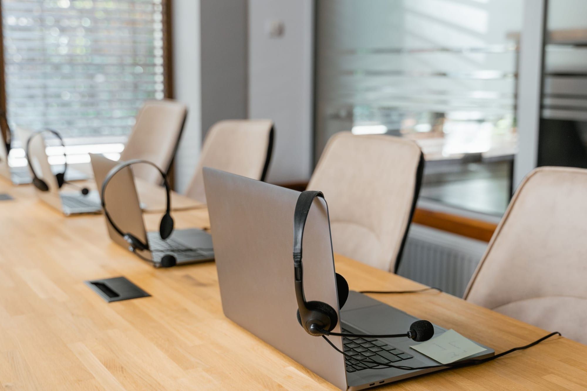 Fila de puestos de trabajo en una mesa de oficina, cada uno con un portátil y unos auriculares con micrófono